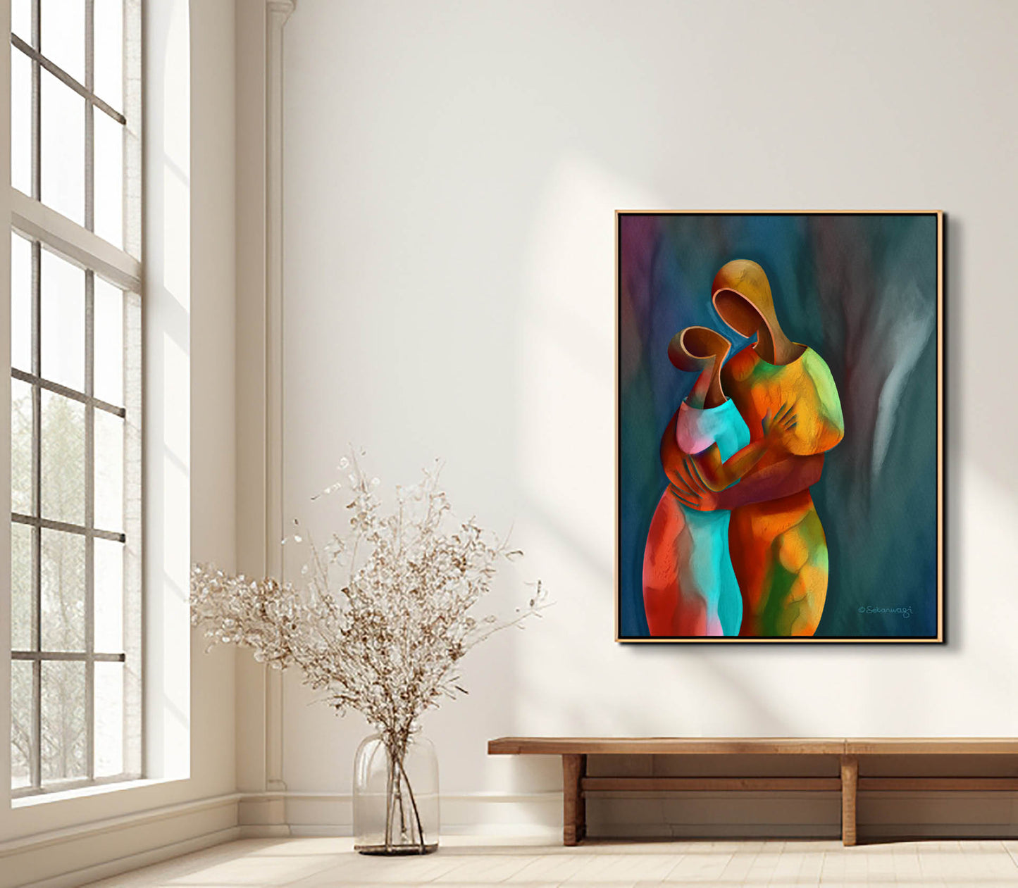 A minimalist room features a large window for natural light. The Confidant - Canvas Art, depicting two embracing figures, hangs on a white wall above a narrow wooden bench, with a delicate dried plant in a vase placed on the floor.