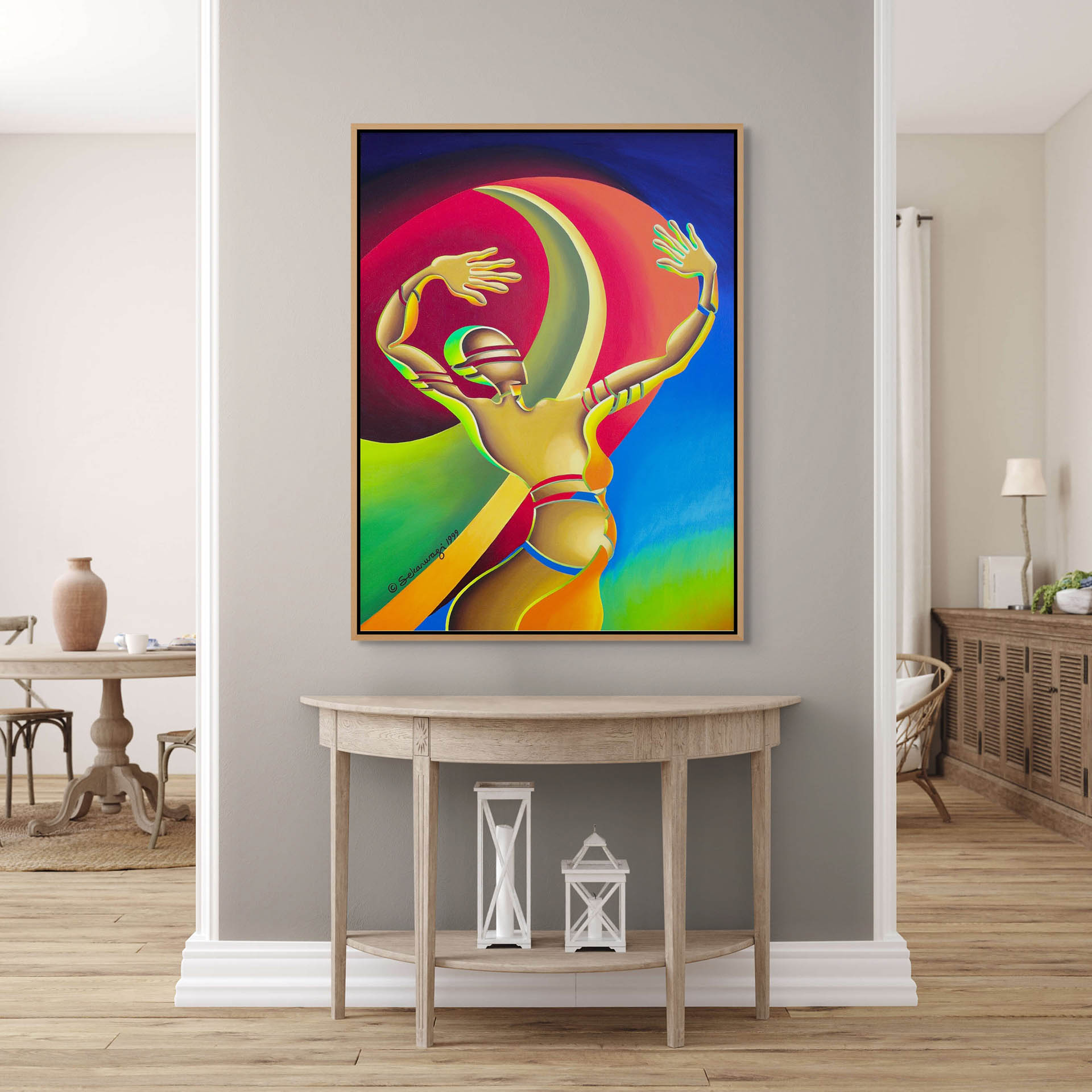A modern living room features The Awakening - Canvas Art, a colorful abstract painting of a figure in motion, mounted on a gray wall. Below it is a wooden console table with two white lanterns. The space reflects minimalist charm with light wood flooring.