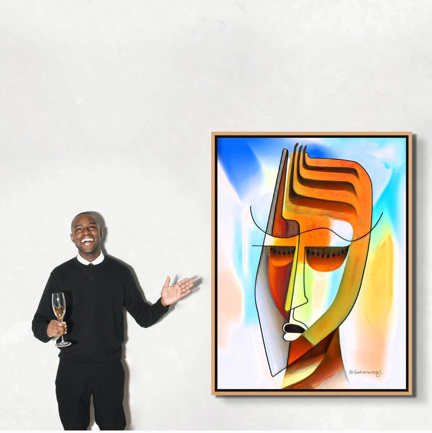 In black attire, a person holds a champagne glass and gestures at Unmasking—a canvas art that explores human identity through geometric faces in vibrant blues, oranges, and yellows. A plain, light-colored wall provides the ideal backdrop for this striking piece.