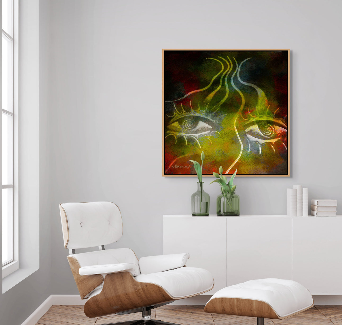 A modern living room showcases a white lounge chair and ottoman on a wooden base. A white cabinet holds vases with tulips, while above, Burning Desire, an abstract painting from the Contemporary African Minimalist collection, adds intrigue with its eyes and swirling patterns.