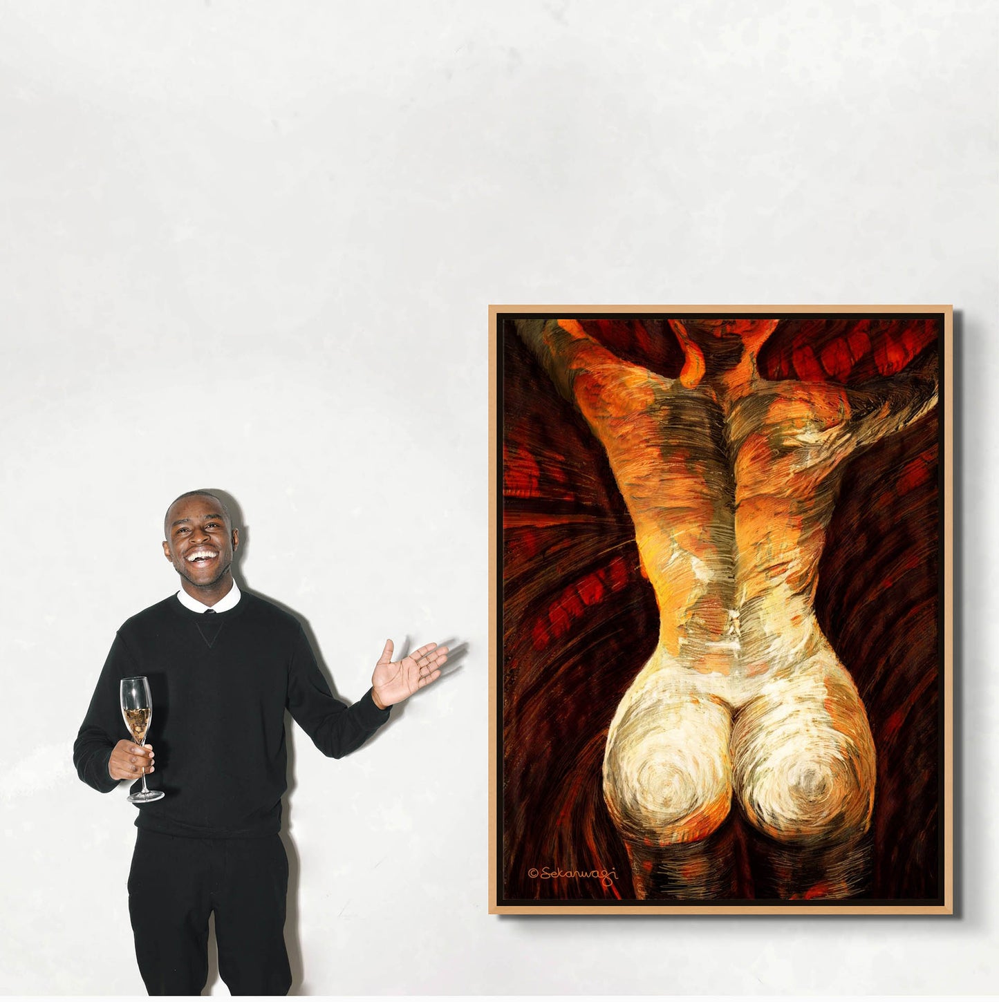 Dressed in black with a white shirt, a person stands smiling against a white wall, holding a champagne glass. They gesture toward Come As You Are - Canvas Art, an exquisite piece of contemporary African art showing a warm-toned human form in a beautiful brown frame.