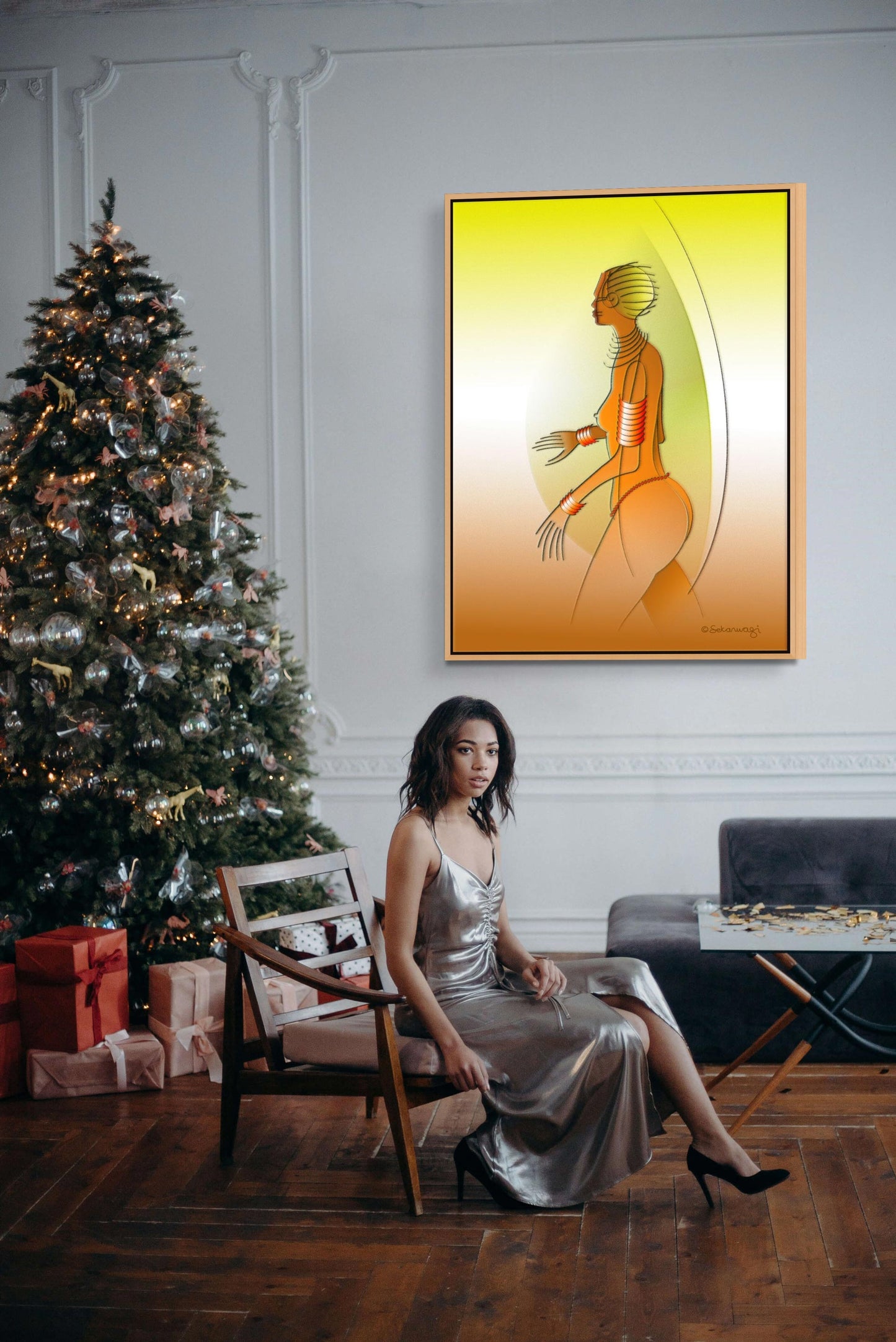 A person in a silver dress sits on a chair beside a decorated Christmas tree and presents. A colorful abstract painting, the Fantasy Woman - Contemporary African Expressionist Canvas Art Print, adorns the wall. The wooden floor enhances the dark couch, completing this magical scene.