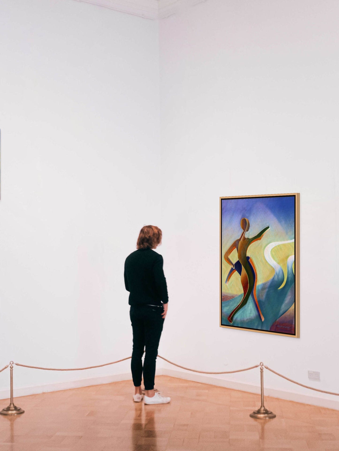 A person with shoulder-length hair, dressed in black and wearing white sneakers, stands in an art gallery admiring the canvas print Fork In The Road showing contemporary African art with an abstract human figure against a white wall. A small rope barrier gently separates the viewer from the artwork.