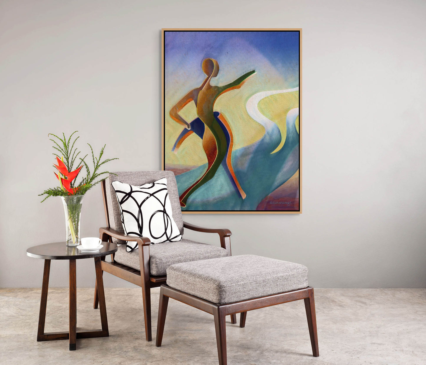 A modern, minimalist room showcases contemporary African art with the Fork In The Road - Canvas Art, a colorful abstract painting of a figure on the wall. A chair and ottoman with gray cushions and a black-and-white patterned pillow sit beside a round side table holding a white teacup and red-flowered vase.