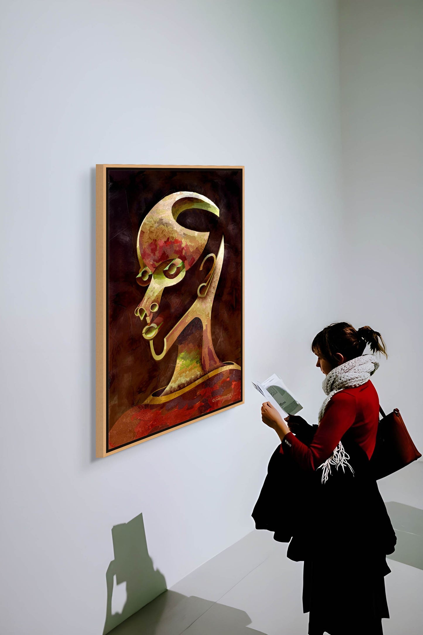 A person with a scarf and dark hair admires Is What You See What You Get? - Canvas Art, a colorful abstract head painting that almost emerges from the gallery wall. They hold a brochure and bag while overhead lighting casts their shadow on the wall.