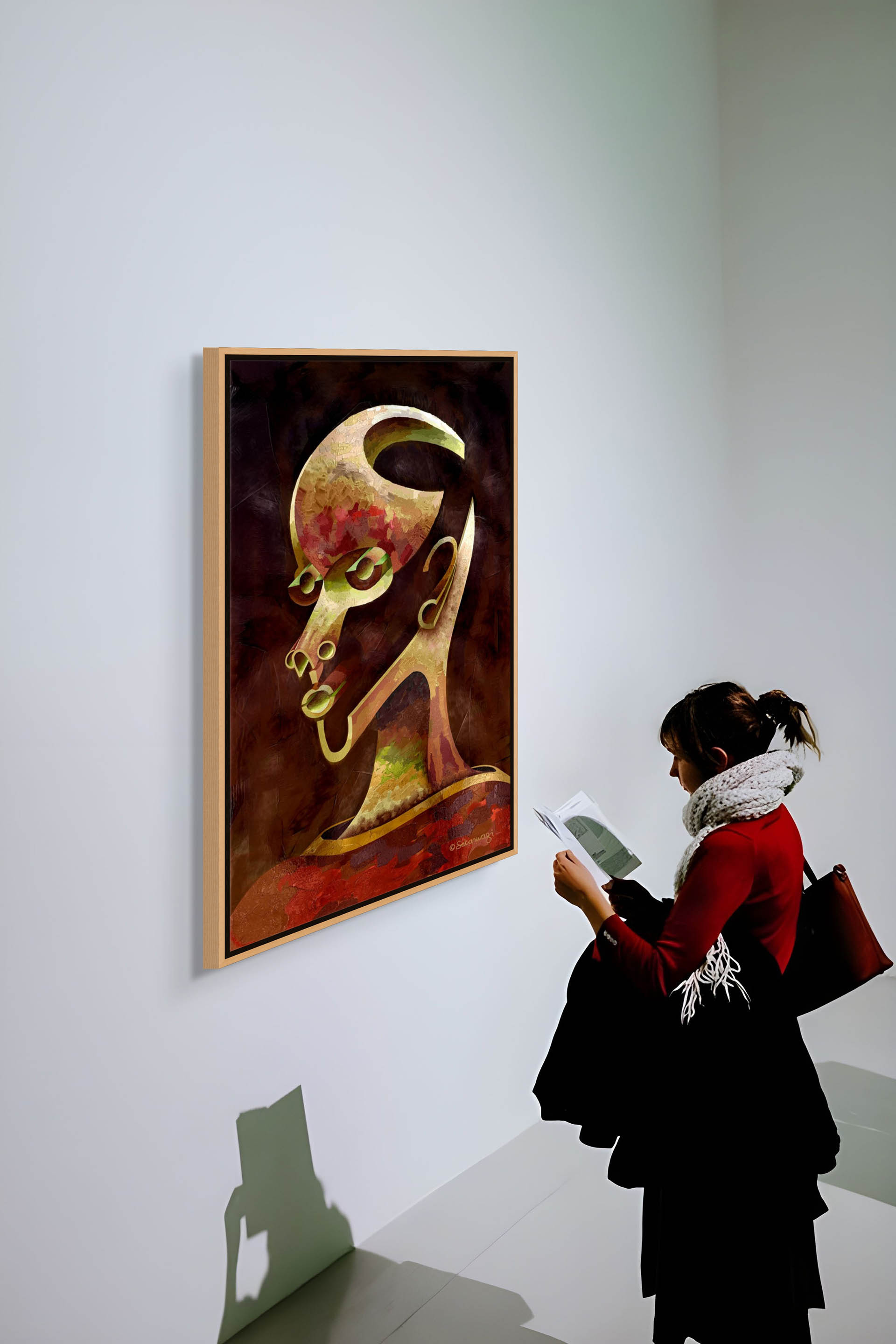 A person with a scarf and dark hair admires Is What You See What You Get? - Canvas Art, a colorful abstract head painting that almost emerges from the gallery wall. They hold a brochure and bag while overhead lighting casts their shadow on the wall.