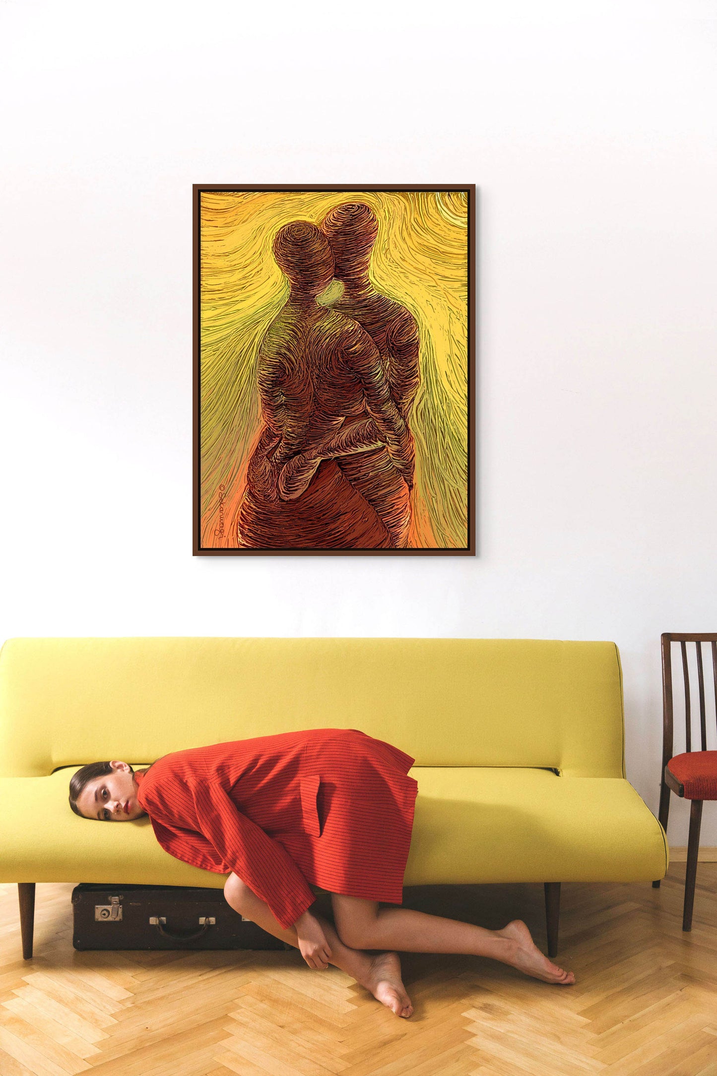 A woman in a red dress leans sideways on a yellow couch in a minimalist room. Above her, Loving Me, Loving You is displayed as a stunning giclee art print on premium quality cotton canvas. A suitcase rests on the floor nearby.