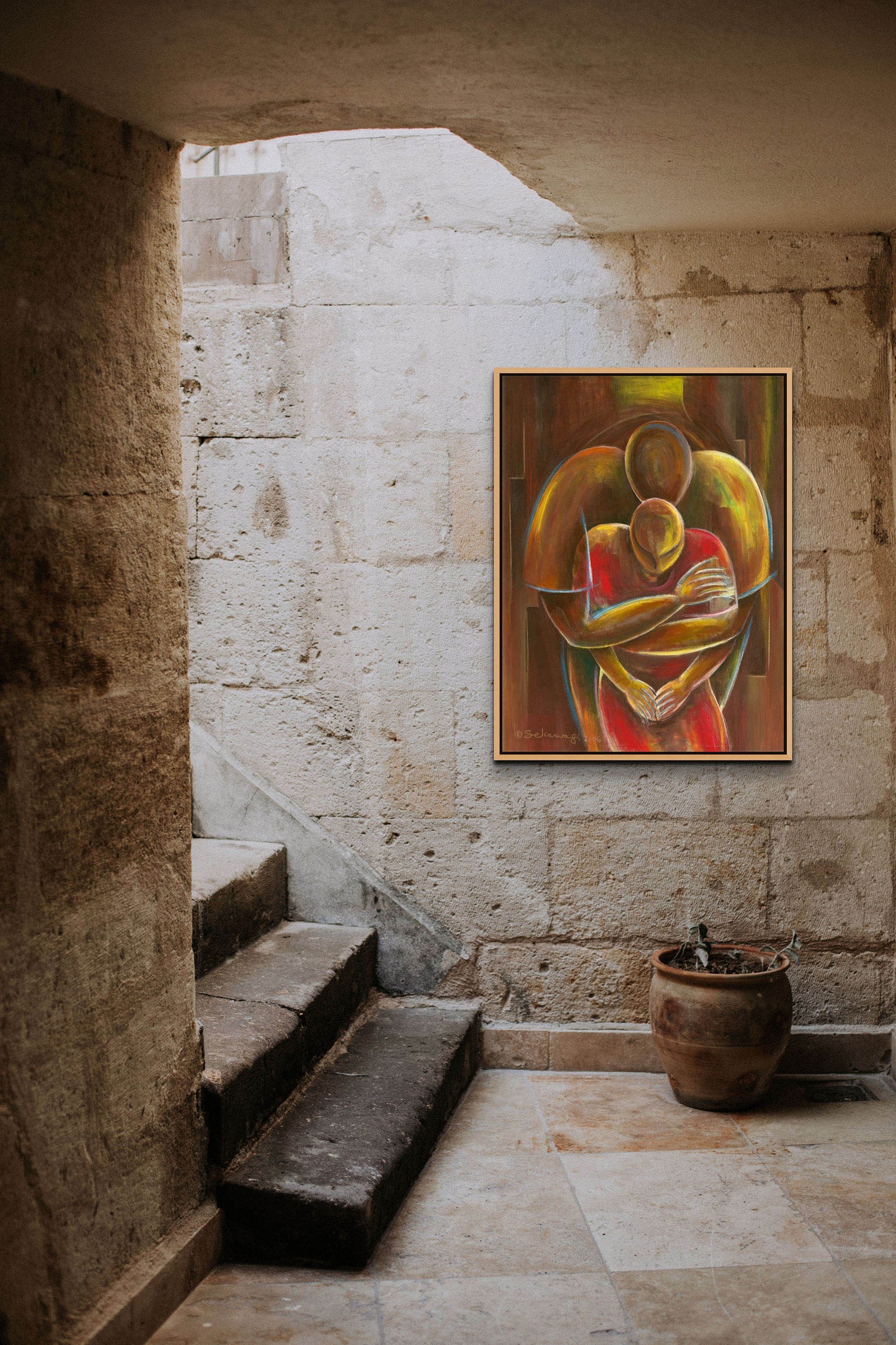 The Nurturing canvas art, a vibrant abstract figure embracing another, is elegantly framed on a stone wall above stairs. Nearby, a potted plant rests on the tiled floor, with natural light beautifully illuminating the ready-to-hang piece in this stone alcove.