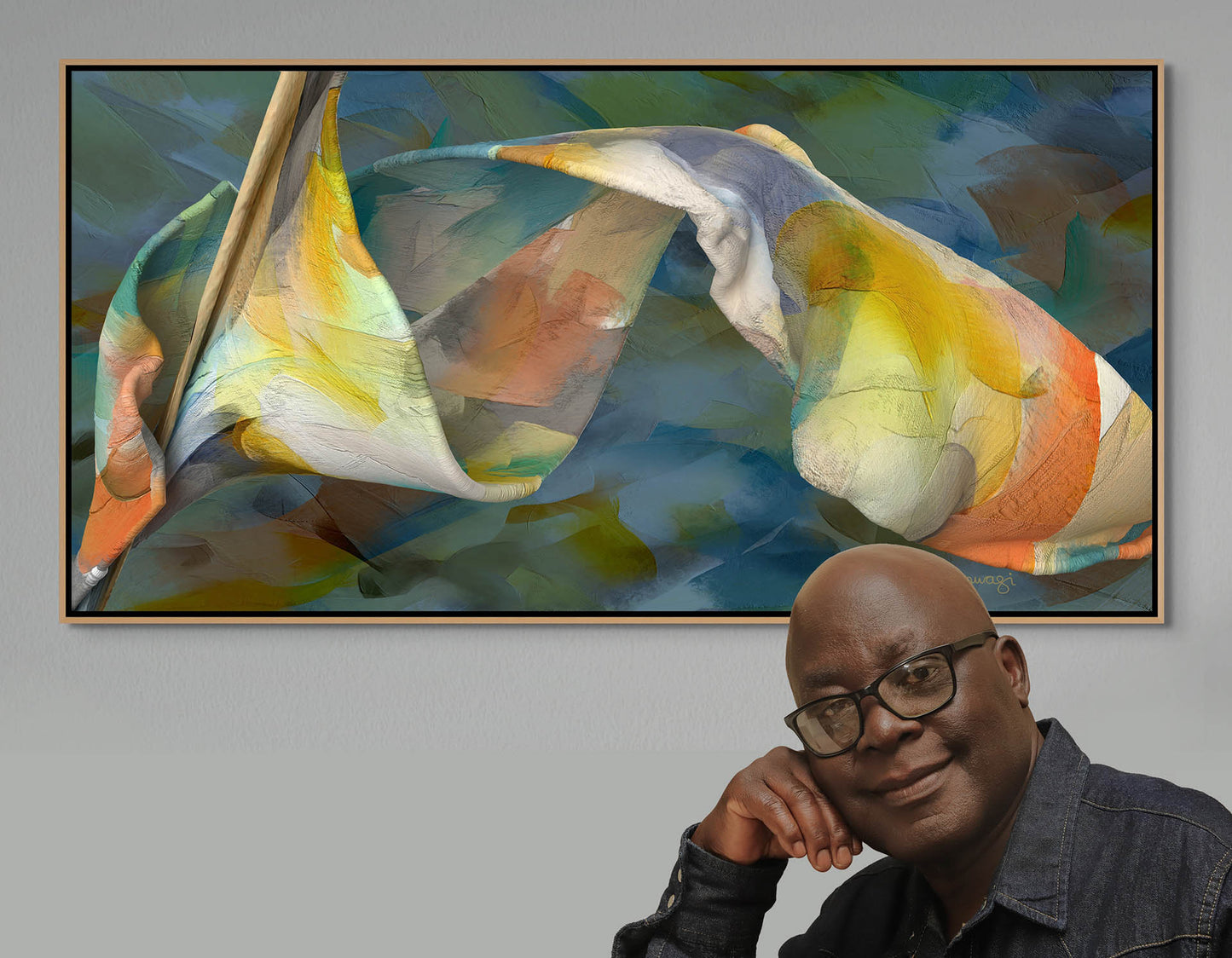 A person in glasses and a dark jacket leans on a counter, smiling. Behind them is Shape Of Unfolding Thought—a colorful, abstract canvas art piece with swirling blue, yellow, and orange shapes. Framed and mounted on a gray wall, it includes free shipping as part of our collection.